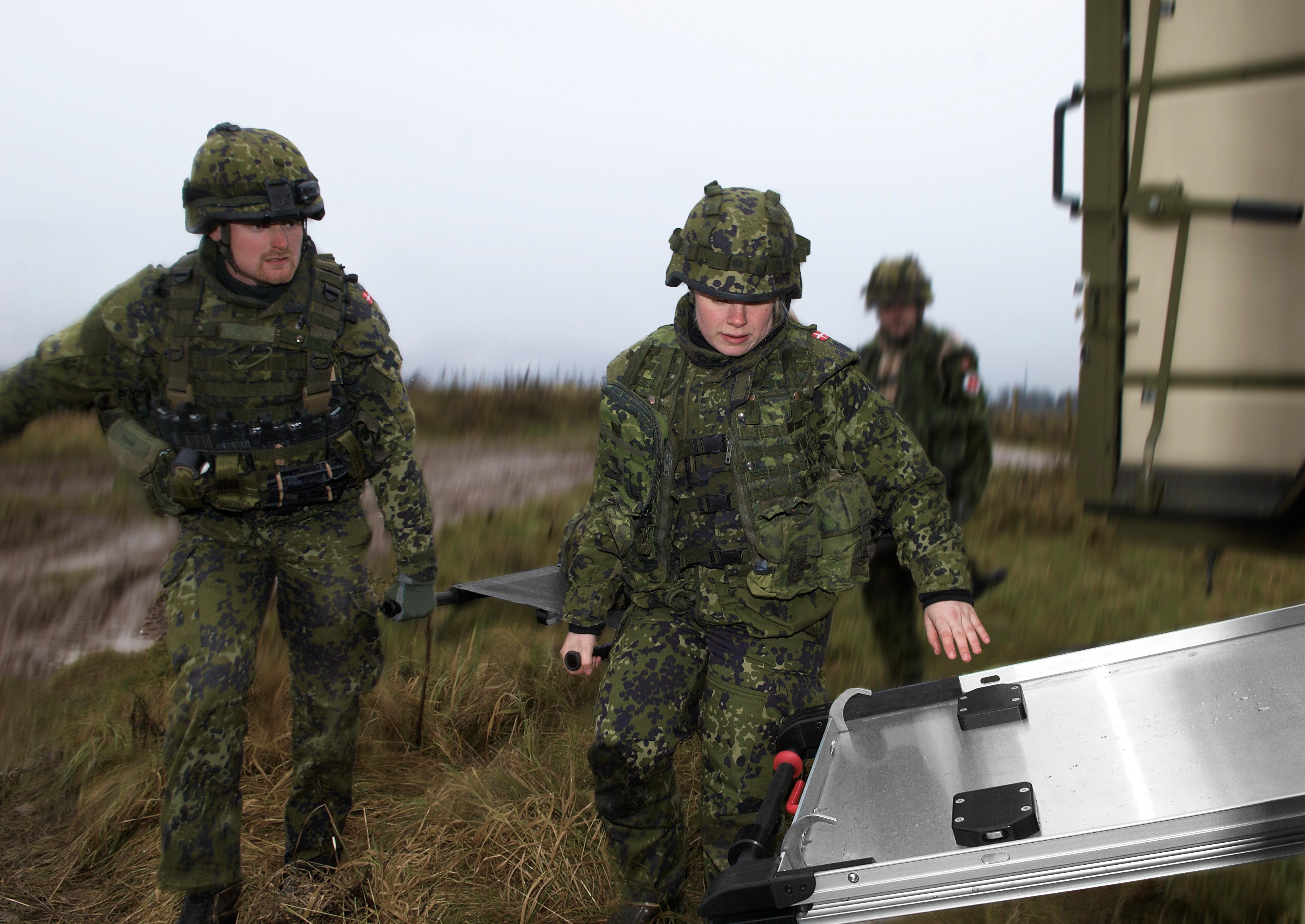 Military medics carrying a patient on stretchers to a stretcher loading system